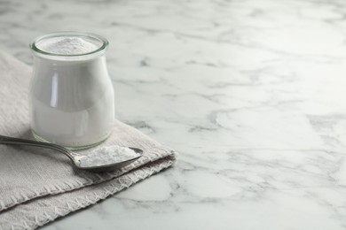 Baking powder in jar and spoon on white marble table, space for text