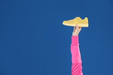 Photo of Young woman holding comfortable shoe on blue background, closeup. Space for text