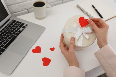 Woman with gift box at white table, closeup. Valentine's day celebration