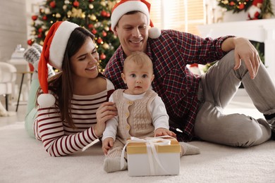 Photo of Happy family with cute baby on floor  in room decorated for Christmas