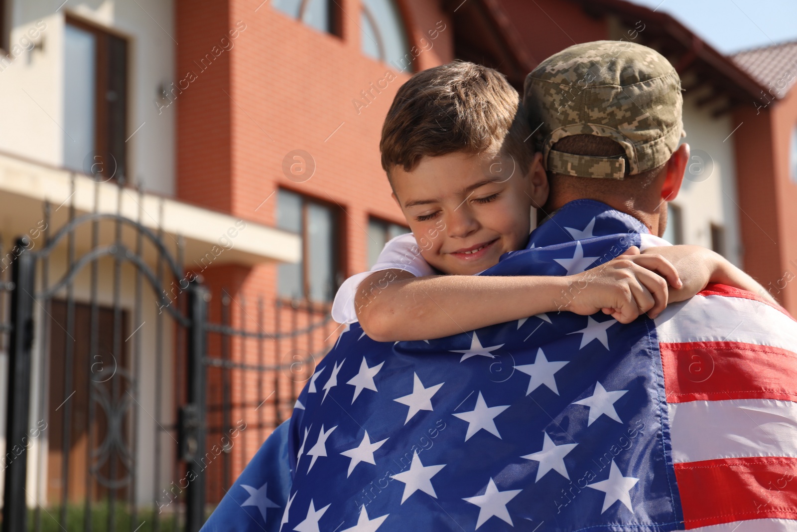 Photo of Soldier with flag of USA and his little son hugging outdoors