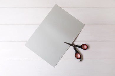 Scissors and paper on white wooden background, top view