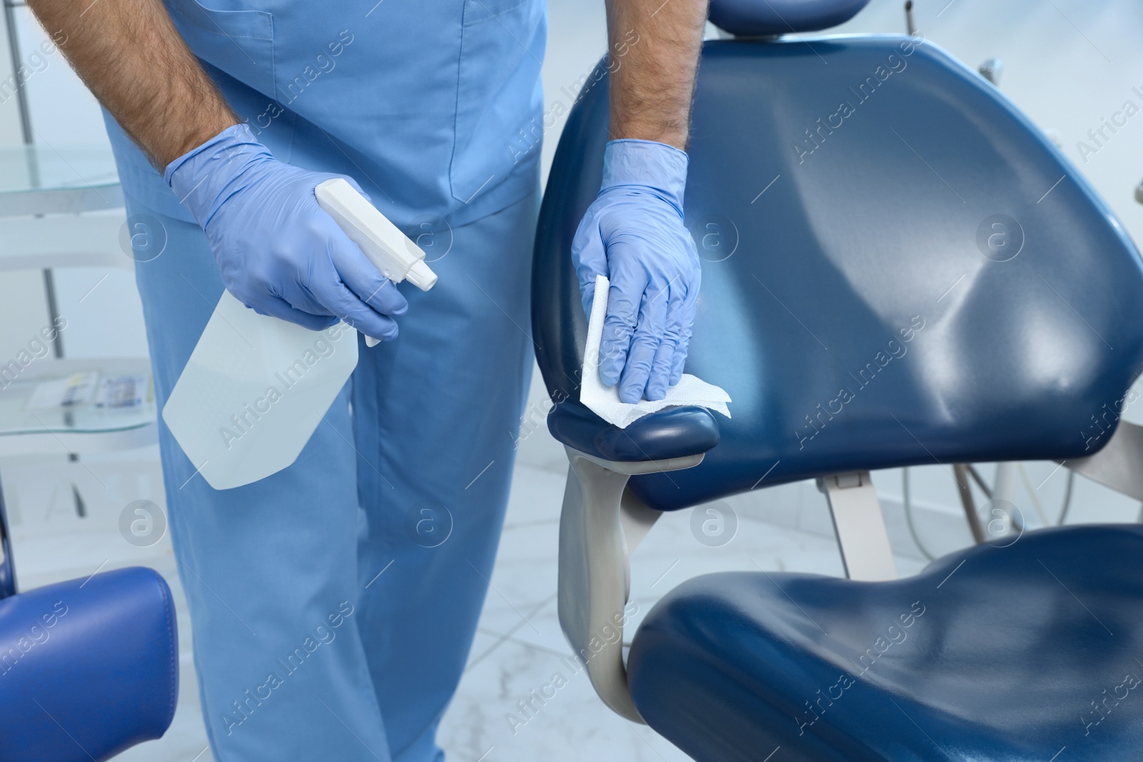 Photo of Professional dentist cleaning workplace with antiseptic in clinic, closeup