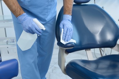 Photo of Professional dentist cleaning workplace with antiseptic in clinic, closeup