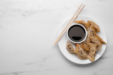 Delicious gyoza (asian dumplings), soy sauce and chopsticks on white marble table, top view. Space for text