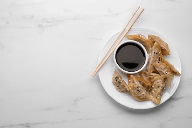 Photo of Delicious gyoza (asian dumplings), soy sauce and chopsticks on white marble table, top view. Space for text