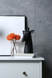 Photo of Stylish decor, vase with flowers and picture on chest of drawers near grey wall indoors. Interior design