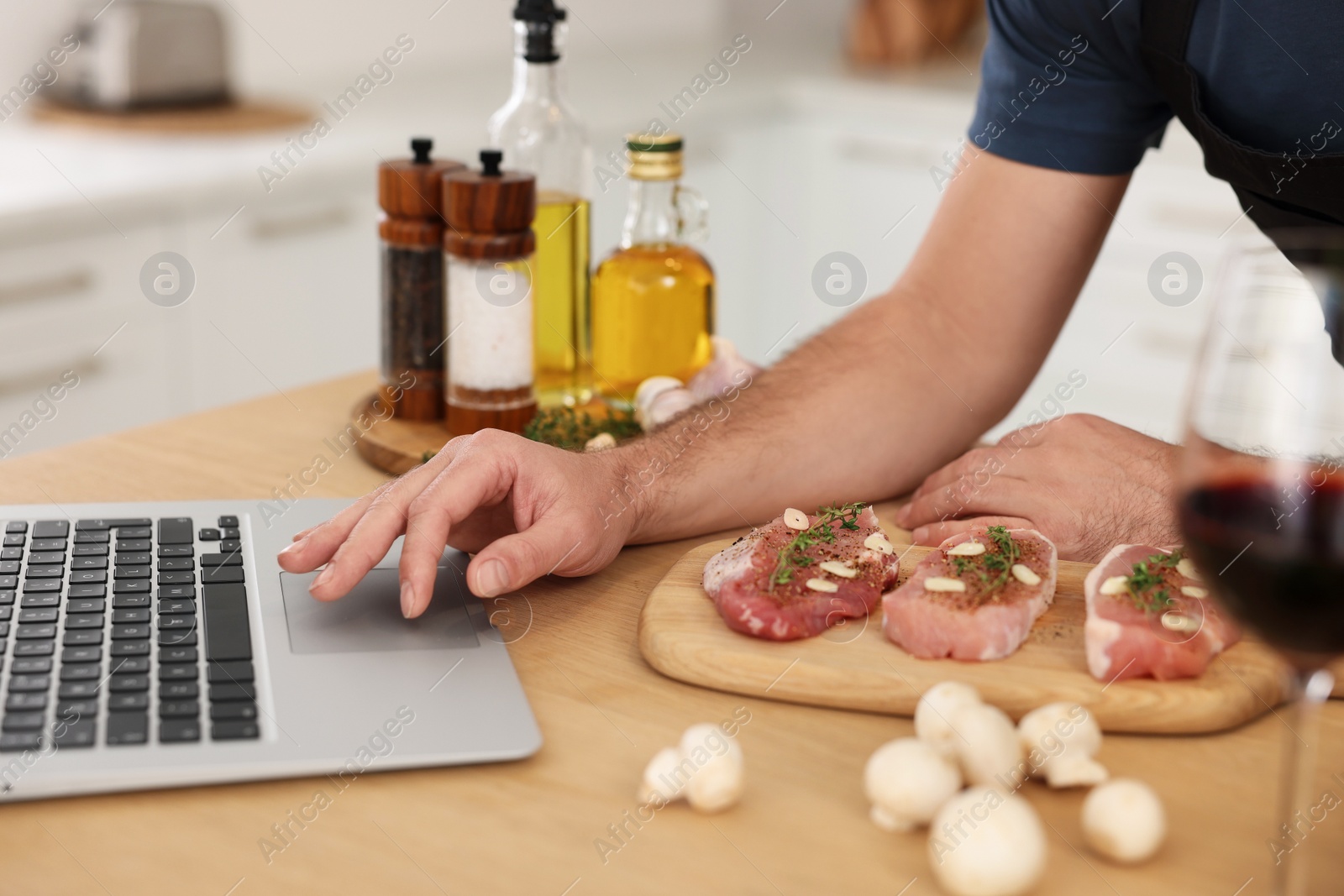 Photo of Man making dinner while watching online cooking course via laptop in kitchen, closeup