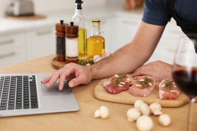 Photo of Man making dinner while watching online cooking course via laptop in kitchen, closeup