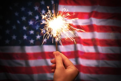 Image of 4th of July - Independence Day of USA. Woman holding burning sparkler against American flag, closeup