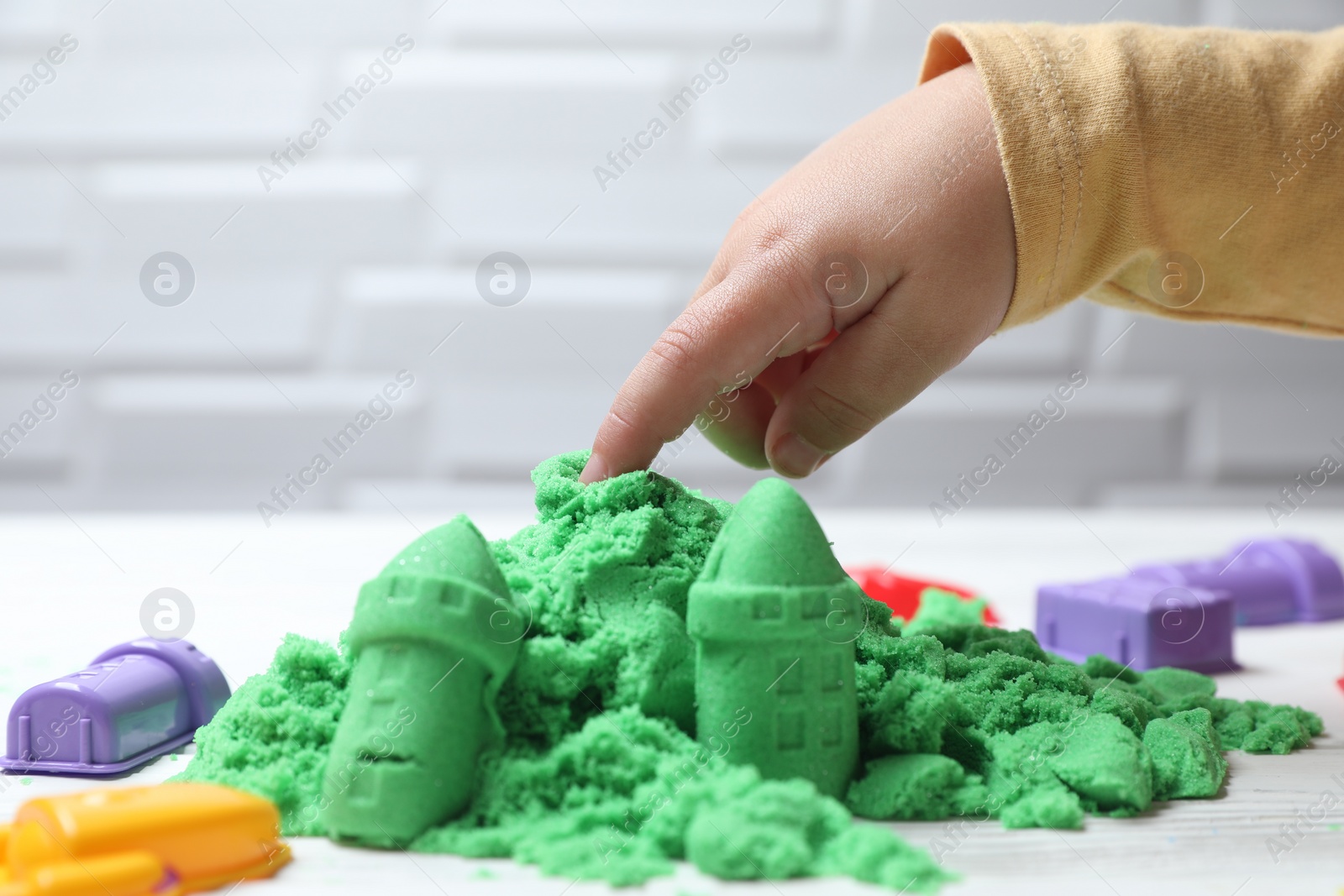 Photo of Little child playing with kinetic sand at white table, closeup