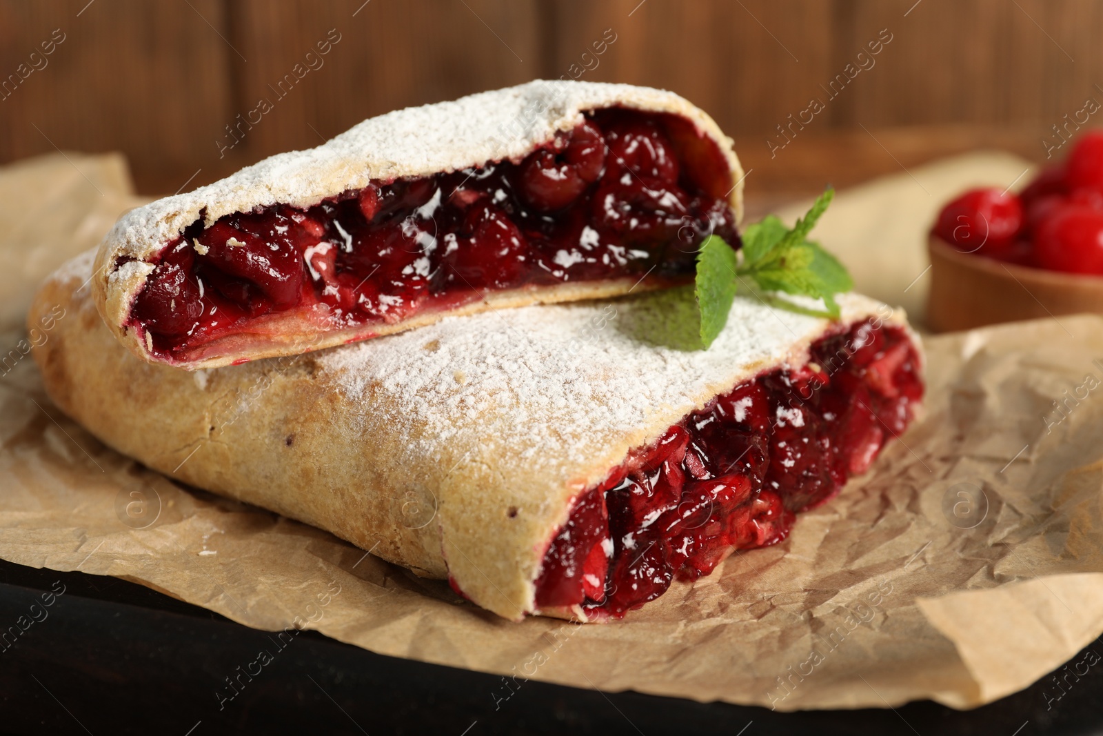 Photo of Delicious strudel with cherries on parchment, closeup