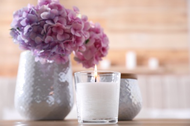 Photo of Burning candle and beautiful flowers on table indoors