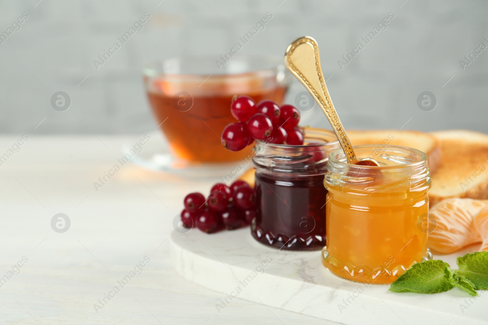 Photo of Jars with different sweet jams and ingredients on white table. Space for text