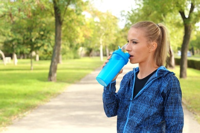 Photo of Woman in sportswear drinking protein shake outdoors. Space for text