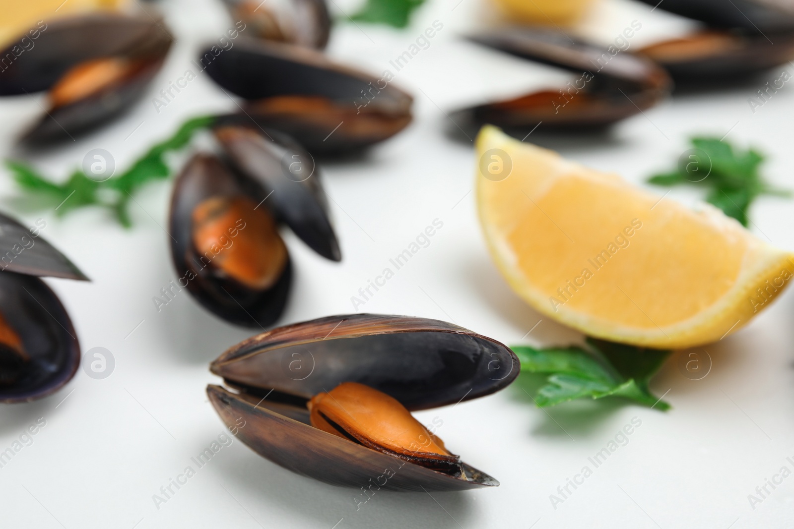 Photo of Cooked mussels with parsley and lemon on white table, closeup