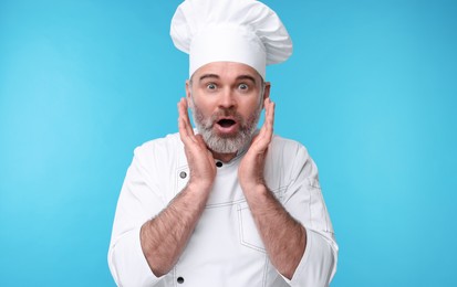 Surprised chef in uniform on light blue background