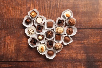 Heart made with delicious chocolate candies on wooden table, top view