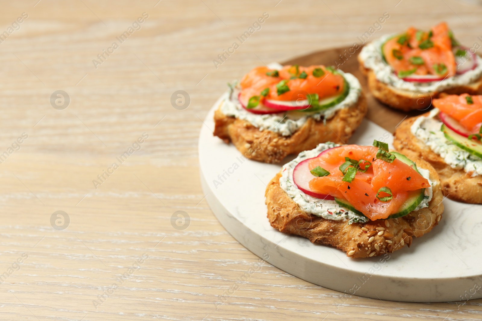 Photo of Tasty canapes with salmon, cucumber, radish and cream cheese on wooden table, space for text