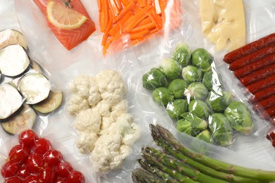 Photo of Different food products in vacuum packs on white wooden table, flat lay