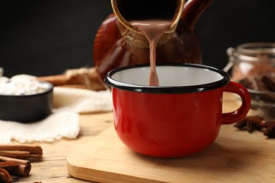 Photo of Pouring tasty hot chocolate into cup at wooden table, closeup