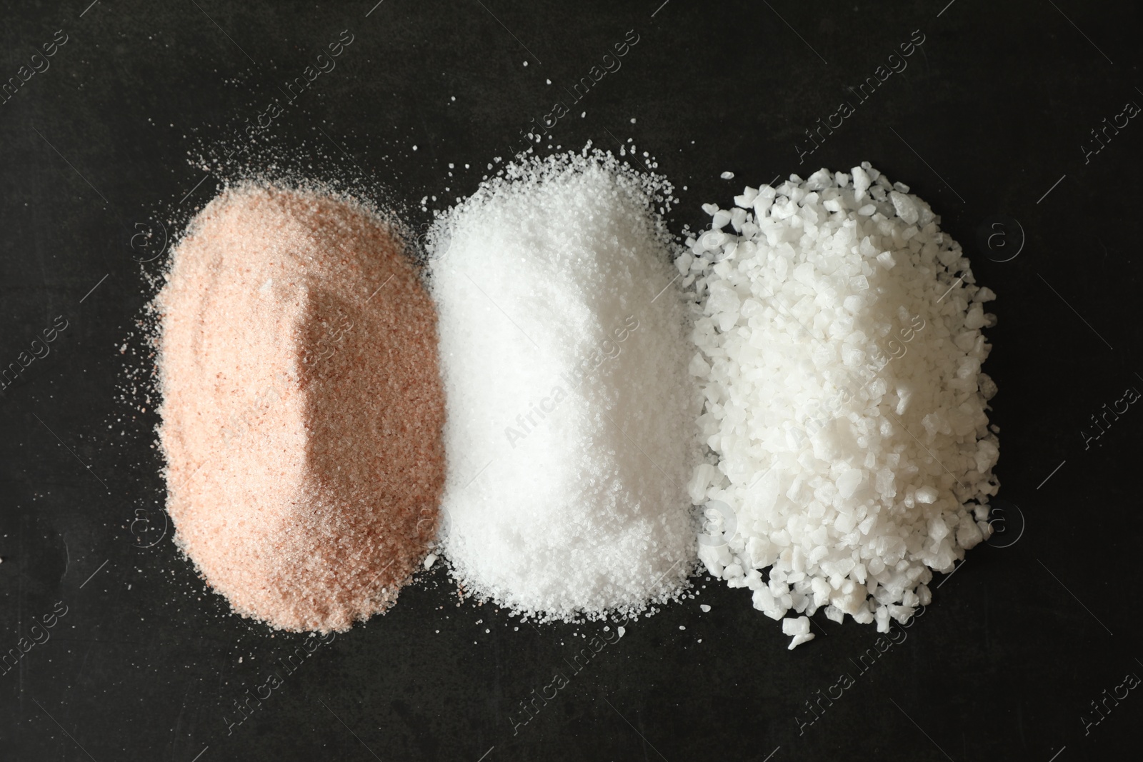 Photo of Different types of organic salt on black table, top view