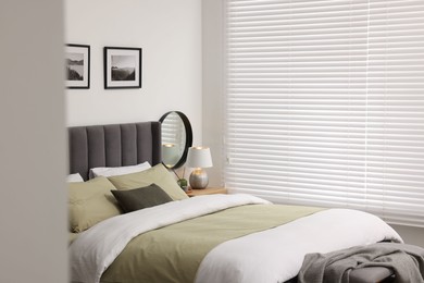 Window with horizontal blinds and comfortable bed in room