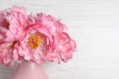 Photo of Beautiful bouquet of pink peonies in vase on white wooden background, closeup. Space for text