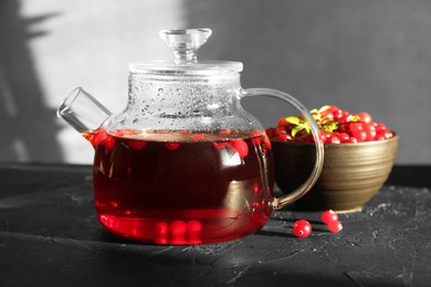 Photo of Tasty hot cranberry tea in teapot and fresh berries on black textured table