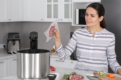 Photo of Woman putting vacuum packed meat into pot with sous vide cooker in kitchen. Thermal immersion circulator