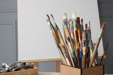 Photo of Easel with blank canvas and different art supplies near grey wall. Space for text