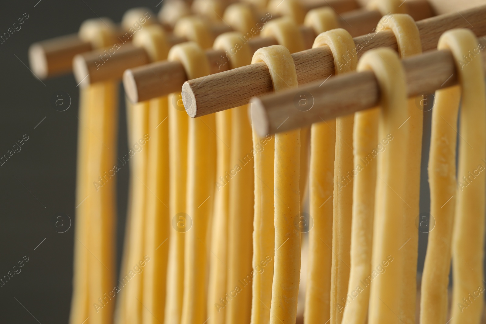 Photo of Homemade pasta drying on wooden rack against dark grey background, closeup