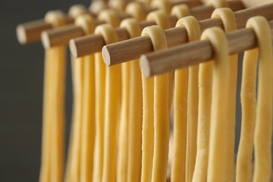 Homemade pasta drying on wooden rack against dark grey background, closeup