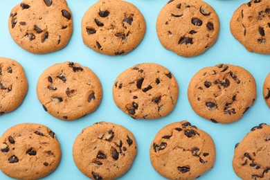 Many delicious chocolate chip cookies on light blue background, flat lay