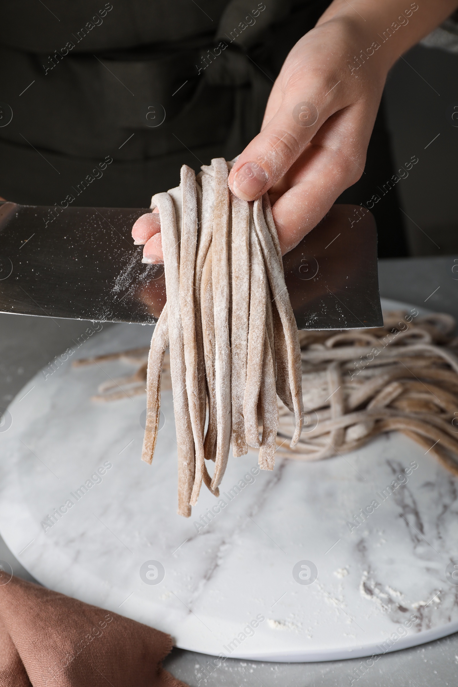 Photo of Woman making soba (buckwheat noodles) at grey table, closeup