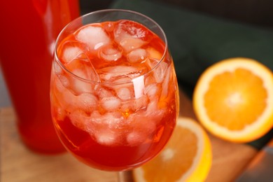 Aperol spritz cocktail and ice cubes in glass on wooden table, closeup