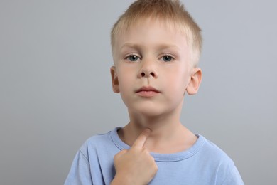 Endocrine system. Little boy doing thyroid self examination on light grey background