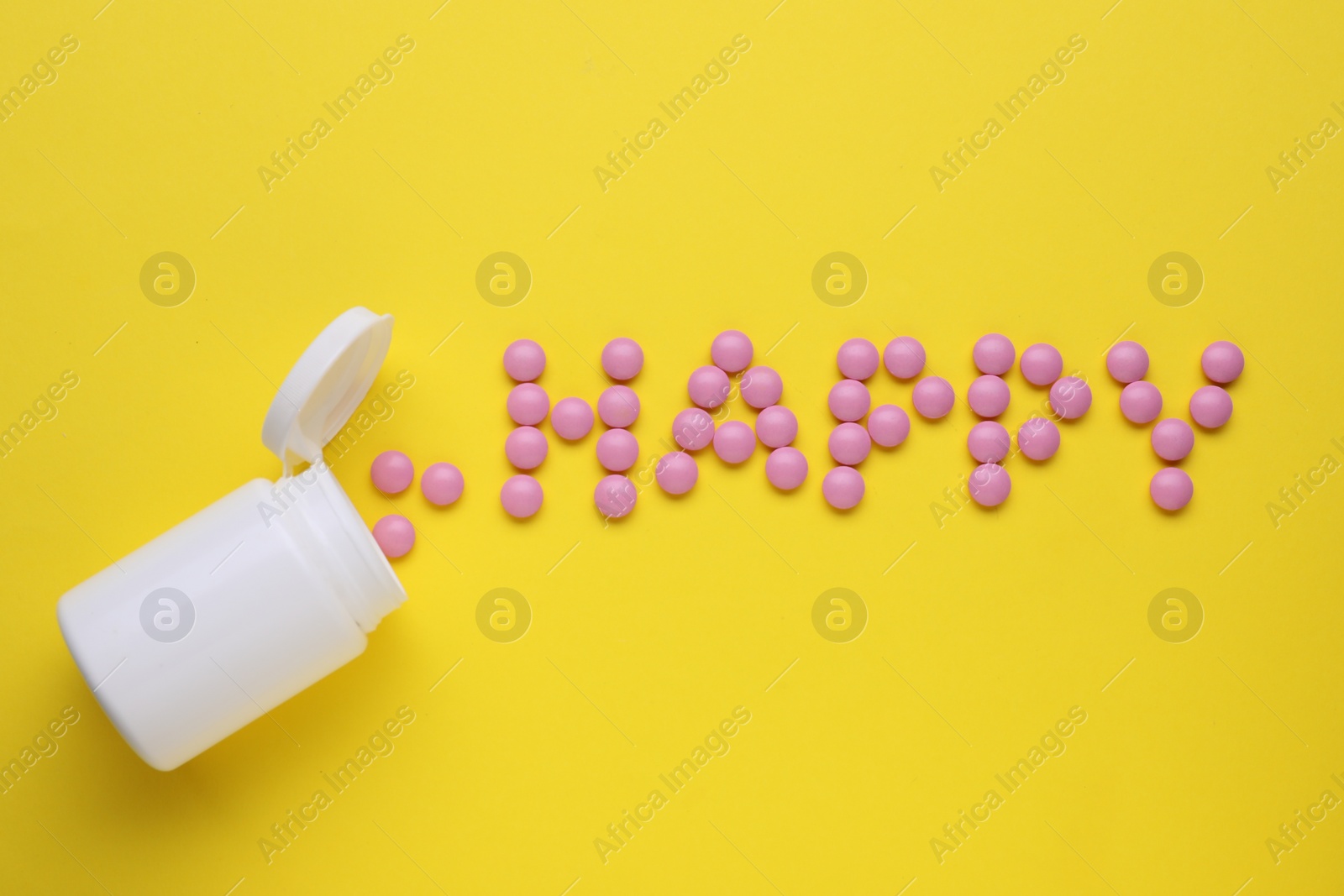 Photo of Word Happy made of pink antidepressants and medical bottle on yellow background, flat lay