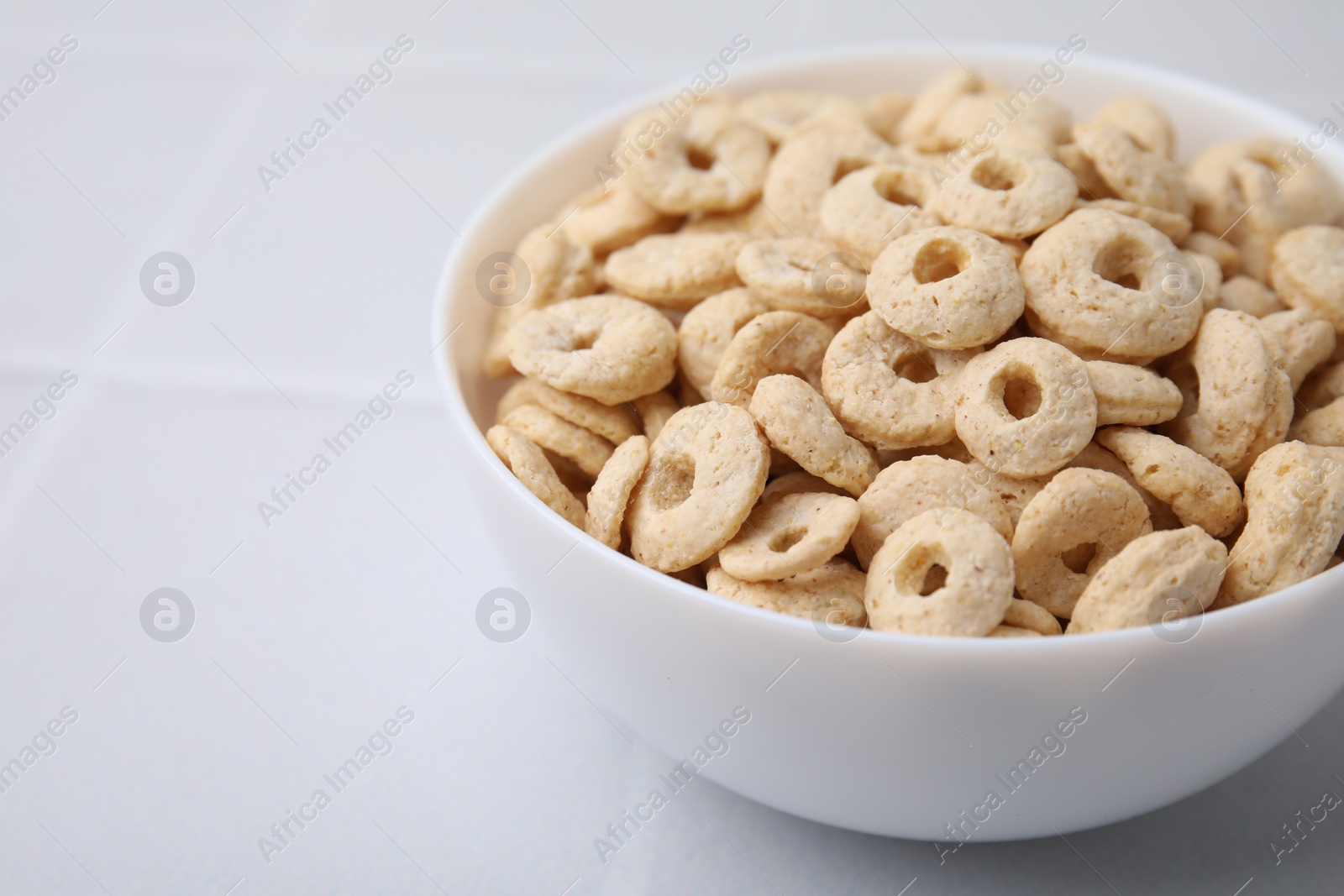 Photo of Tasty cereal rings in bowl on white table, closeup. Space for text