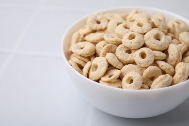 Photo of Tasty cereal rings in bowl on white table, closeup. Space for text