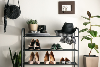 Photo of Black shelving unit with shoes and different accessories near white wall in hall