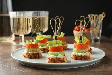 Tasty canapes with salmon, cucumber, bread and cream cheese on wooden table, closeup