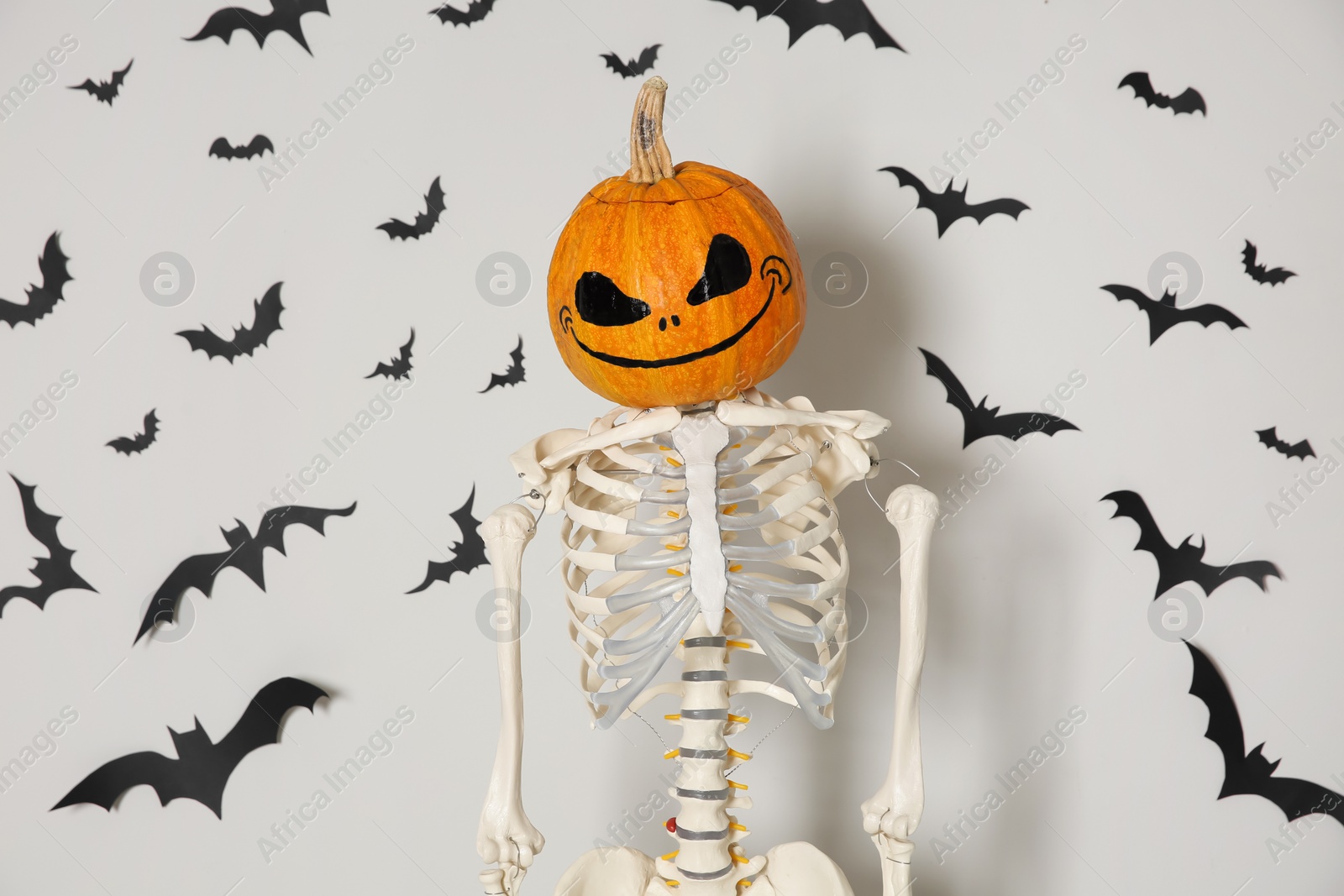 Photo of Skeleton with pumpkin head and paper bats on white wall