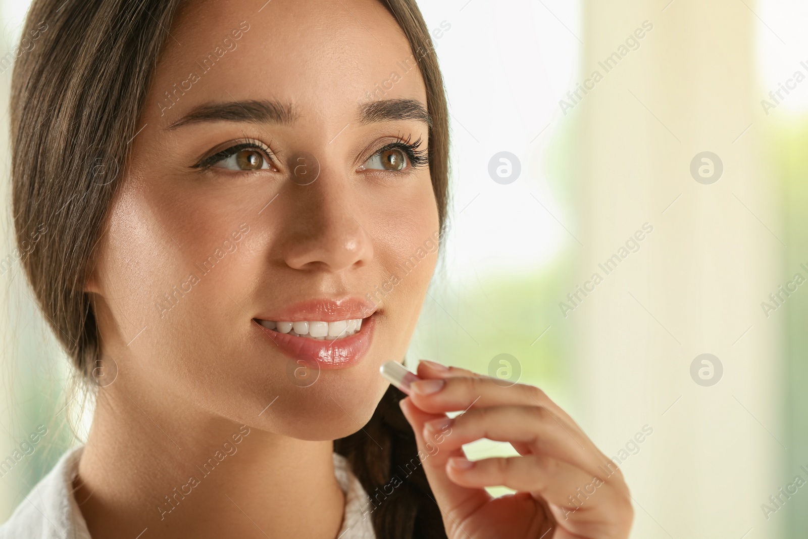 Photo of Young woman taking dietary supplement pill on blurred background, closeup. Space for text