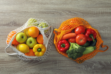 Net bags with vegetables and fruits on wooden table, flat lay