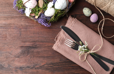 Cutlery set with quail eggs on wooden table, flat lay. Easter celebration