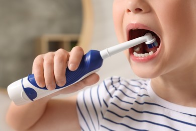 Little girl brushing her teeth with electric toothbrush indoors, closeup