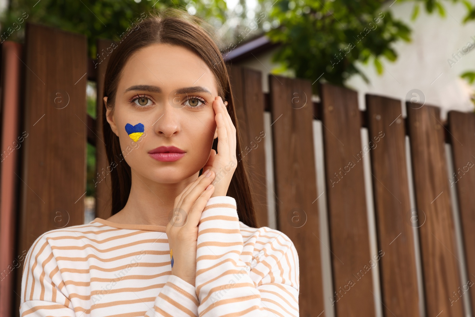 Photo of Young woman with drawing of Ukrainian flag on face outdoors, space for text
