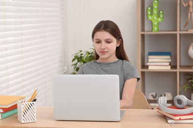 Cute girl using laptop at desk in room. Home workplace