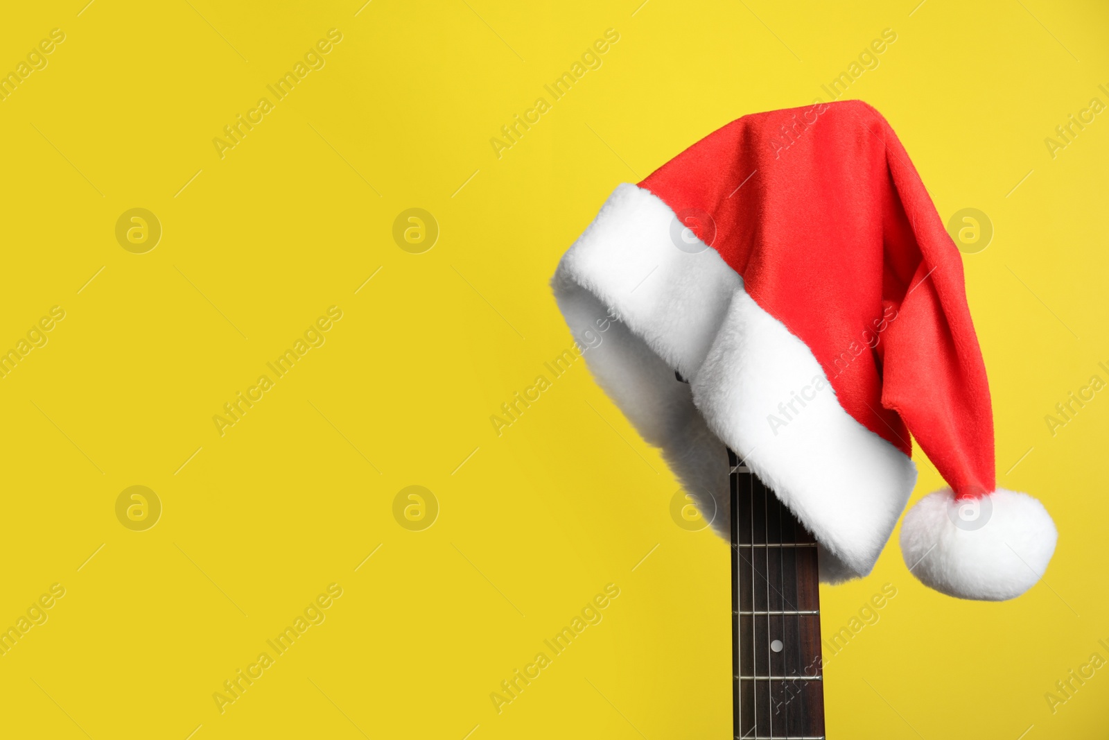 Photo of Guitar with Santa hat on yellow background, space for text. Christmas music concept